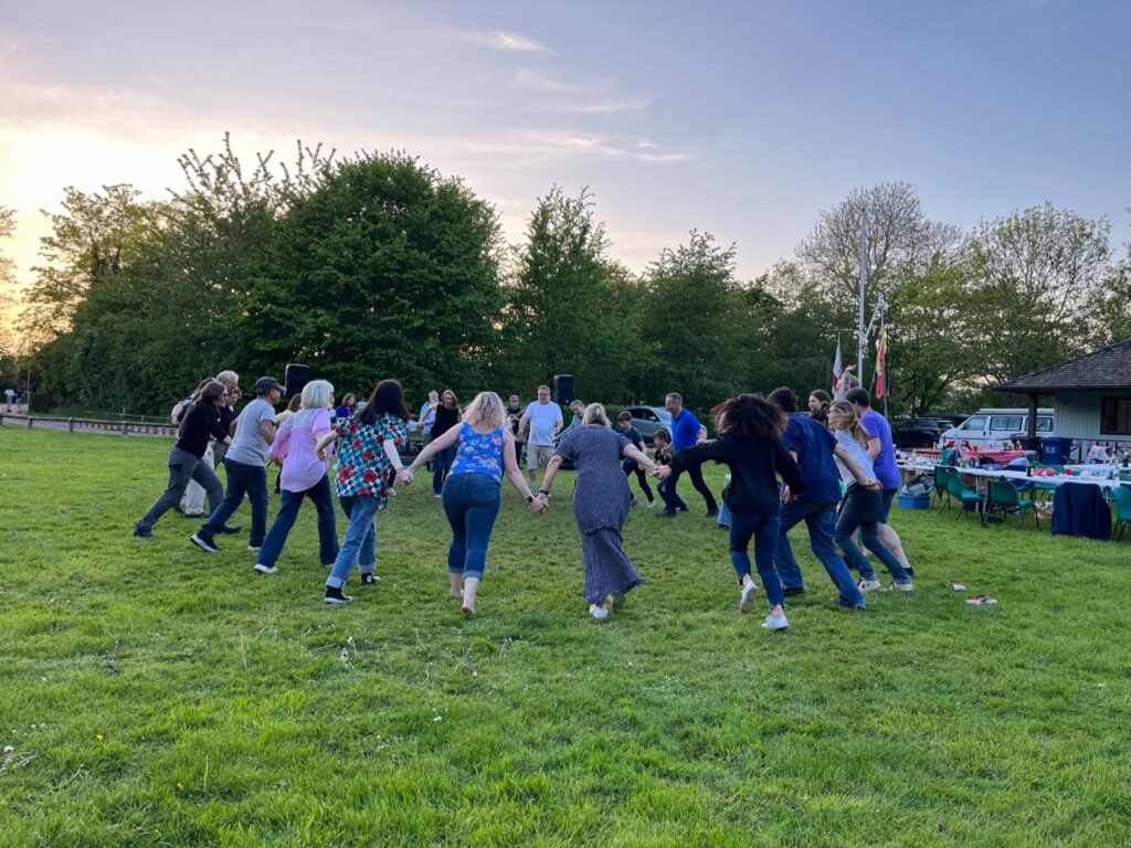 a group of dancers in a ring dancing at dusk on a grass field