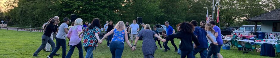 a group of dancers in a ring dancing at dusk on a grass field