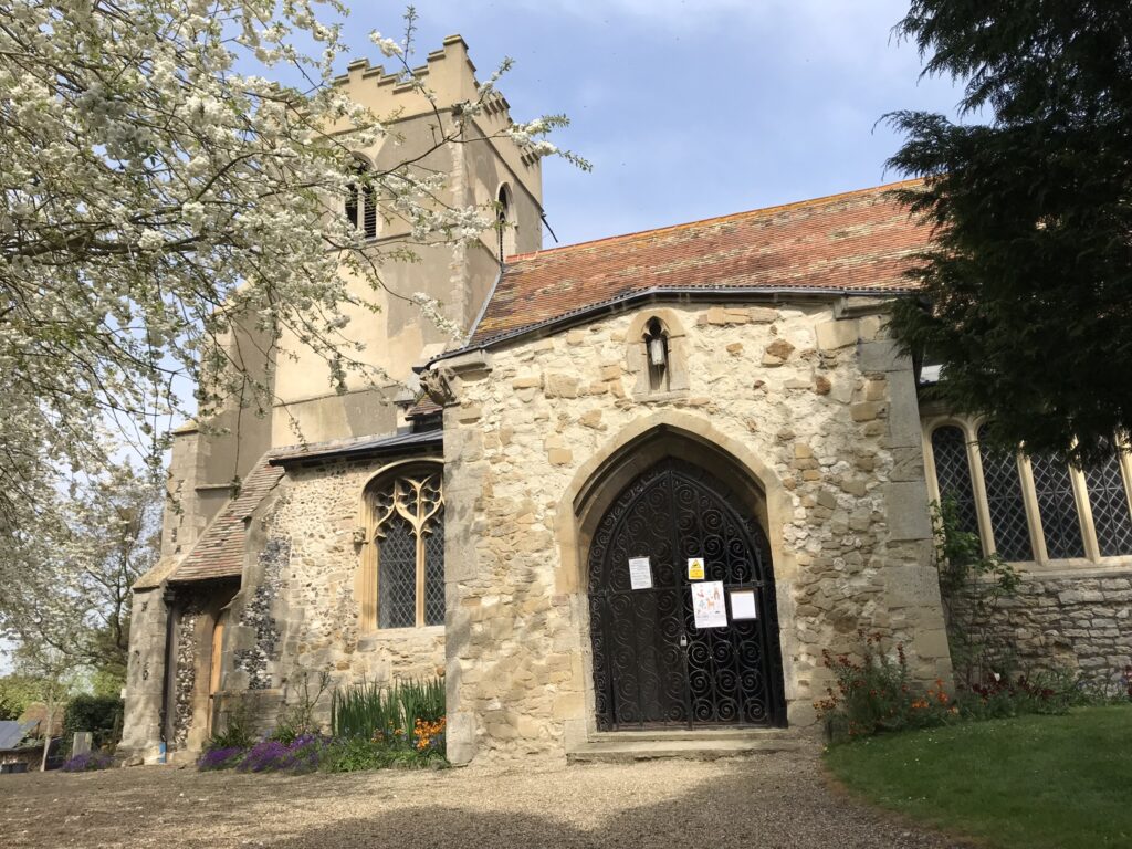 A stone built church porch in the sunshine surrounded by trees