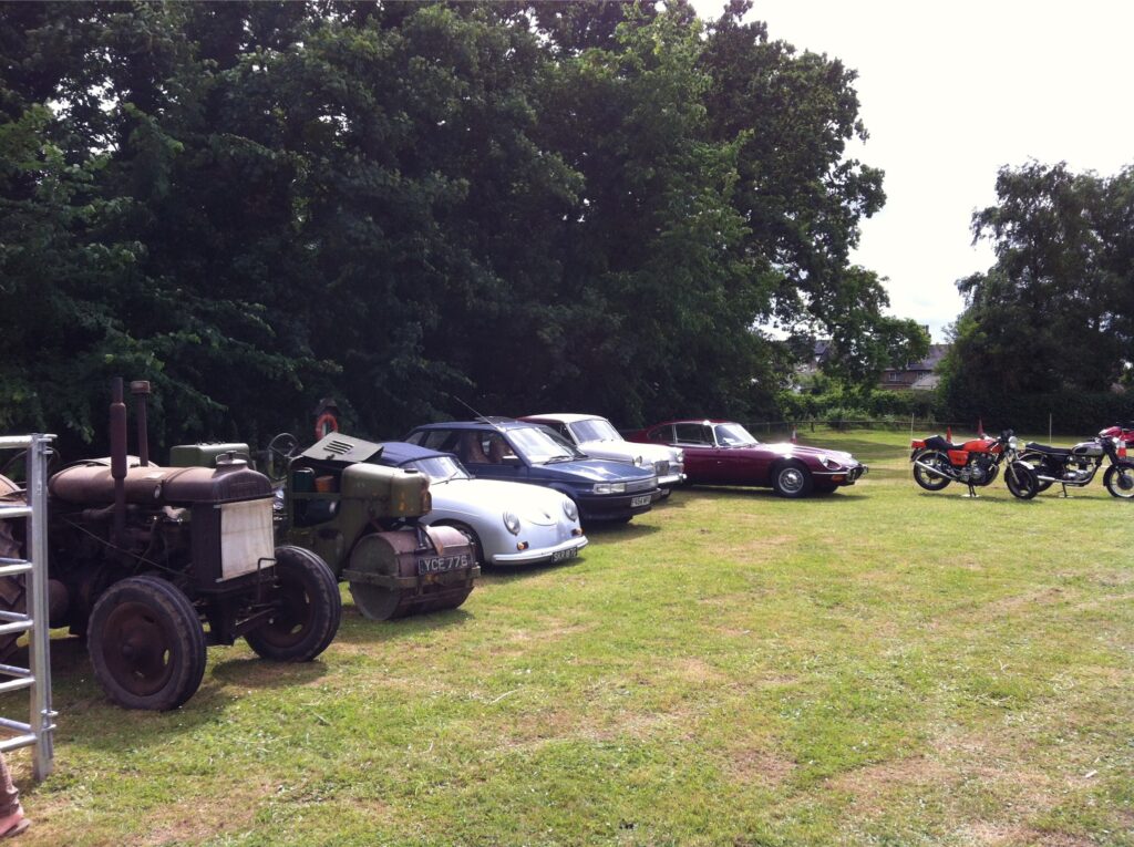 A line of vintage cars and tractors on a village green