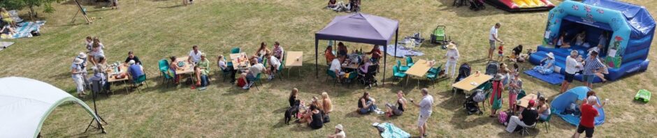 An overhead drone shot of a field with bounch castles and people sat enjoying the sunshine